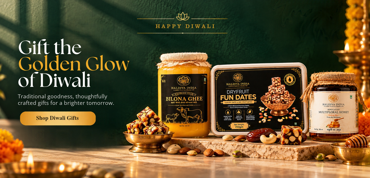 A festive Diwali gift set from Happy Diwali, featuring a jar of Bilona Ghee, a box of Dr. Fruit Fun Dates, and a jar of Amla Chutney, styled on a marble surface with nuts, dried fruits, and candles against a dark green background.